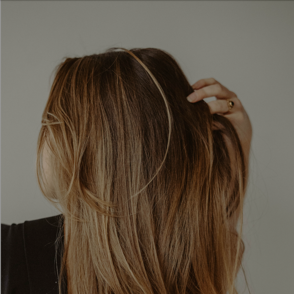 woman running fingers through brown hair after using hair loss products